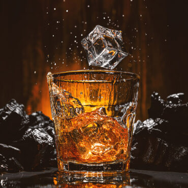 ice cubes fall into a glass with a brown alcoholic drink
