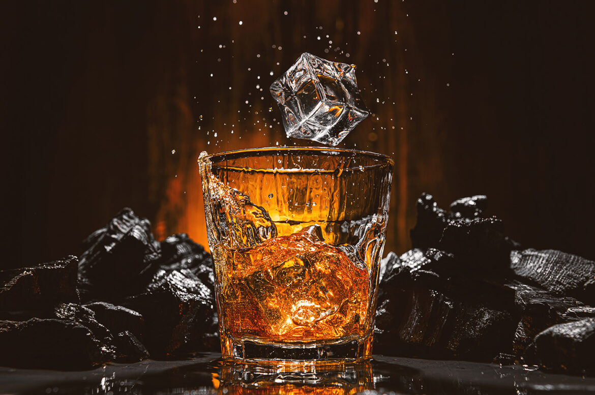 ice cubes fall into a glass with a brown alcoholic drink